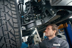 Technician inspecting a car's front suspension for the cause of a clunking noise