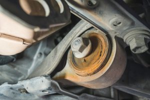 Worn front suspension control arm bushing showing deterioration and corrosion
